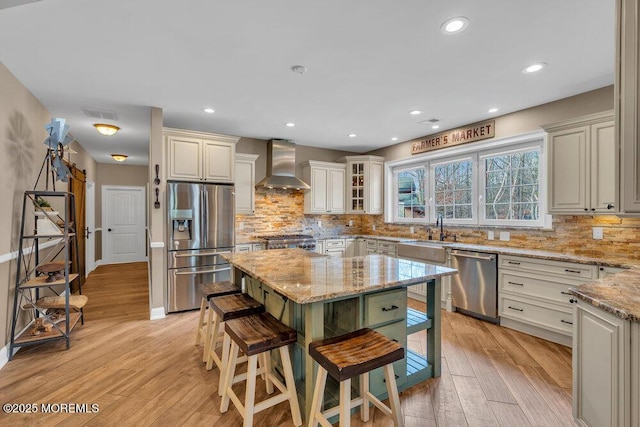 kitchen featuring light wood-type flooring, wall chimney range hood, light stone counters, a sink, and stainless steel appliances