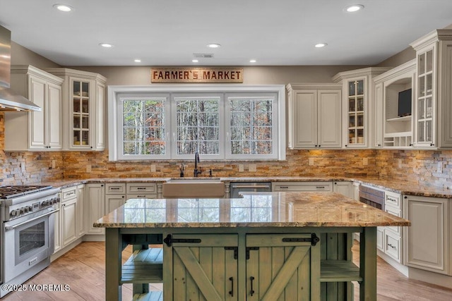 kitchen with wall chimney exhaust hood, decorative backsplash, stainless steel appliances, light wood finished floors, and a sink