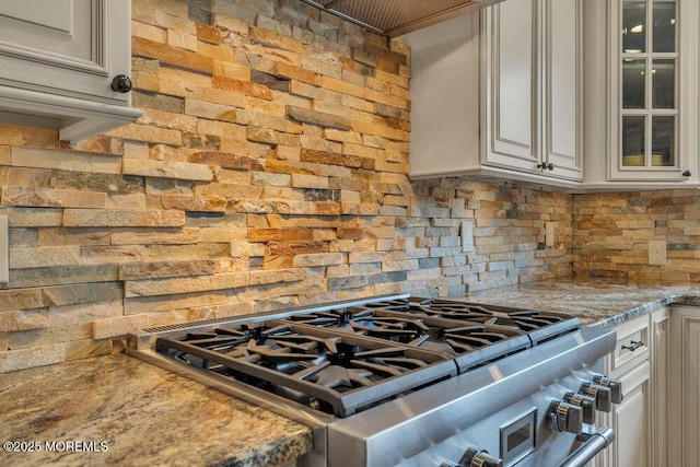 kitchen with tasteful backsplash, glass insert cabinets, double oven range, and light stone counters