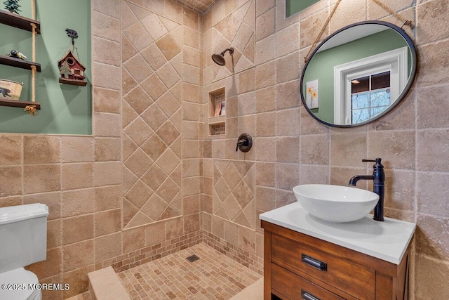 bathroom with toilet, tile walls, tiled shower, and vanity