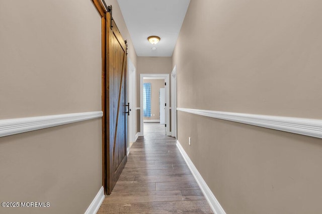 corridor featuring hardwood / wood-style floors, baseboards, and a barn door