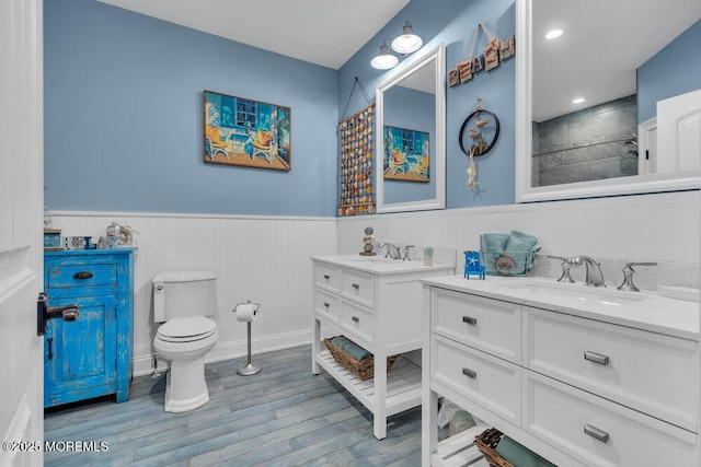 full bath with two vanities, wood finished floors, a sink, and a wainscoted wall