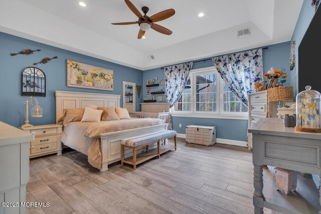bedroom with visible vents, baseboards, a raised ceiling, light wood-type flooring, and recessed lighting