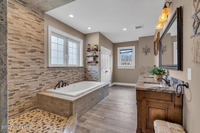 full bathroom with a bath, vanity, visible vents, wood finished floors, and baseboards