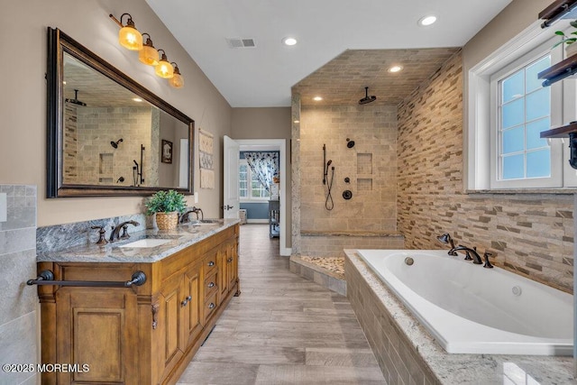 bathroom featuring a tile shower, a bath, a sink, and visible vents
