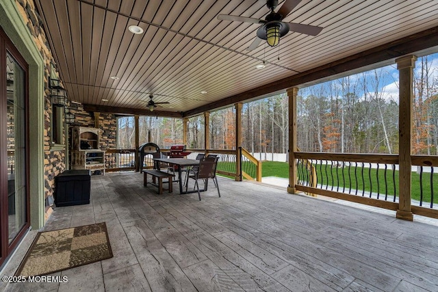 unfurnished sunroom featuring a deck, ceiling fan, an outdoor stone fireplace, and outdoor dining area