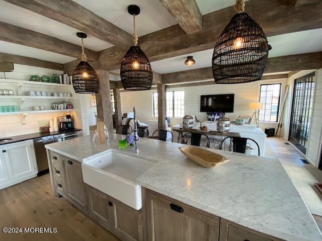 kitchen with a sink, stainless steel dishwasher, beamed ceiling, pendant lighting, and light wood-style flooring