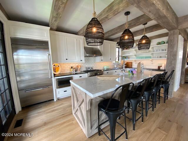 kitchen featuring stainless steel built in refrigerator, stove, light wood-style floors, and extractor fan