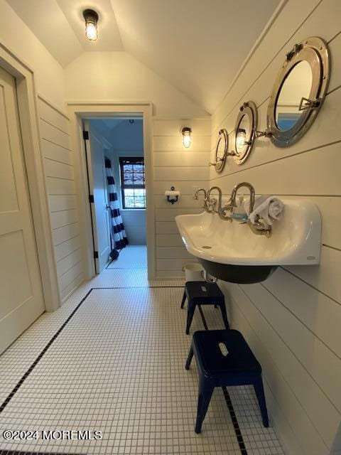 bathroom with a sink, wood walls, and vaulted ceiling