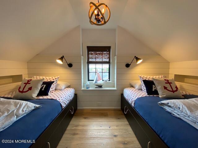 bedroom with light wood finished floors, a chandelier, wooden walls, and vaulted ceiling