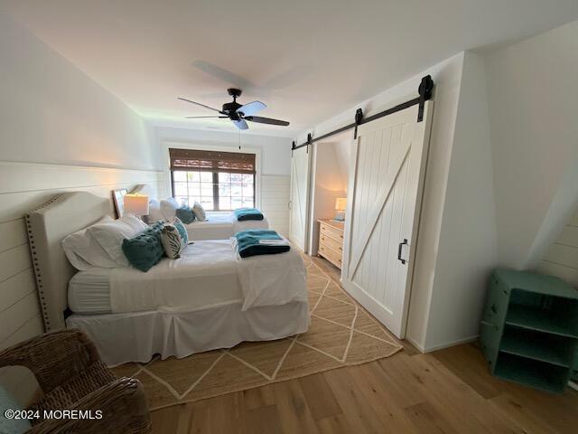 bedroom with light wood-type flooring, a ceiling fan, and a barn door
