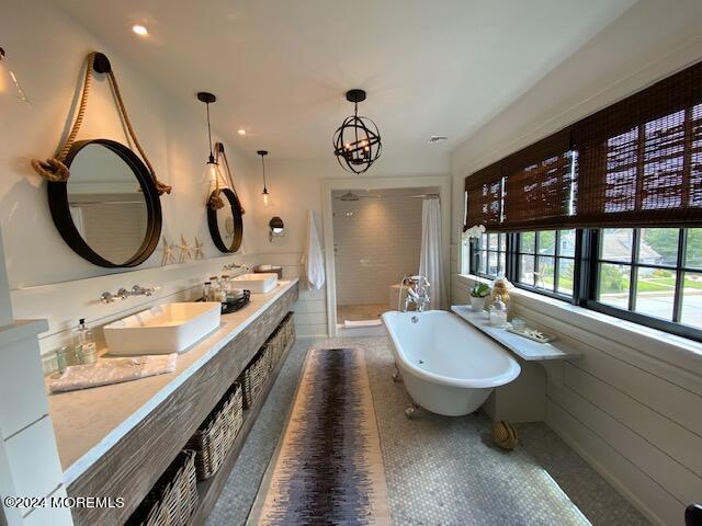 full bath featuring a soaking tub, a chandelier, walk in shower, wainscoting, and a sink