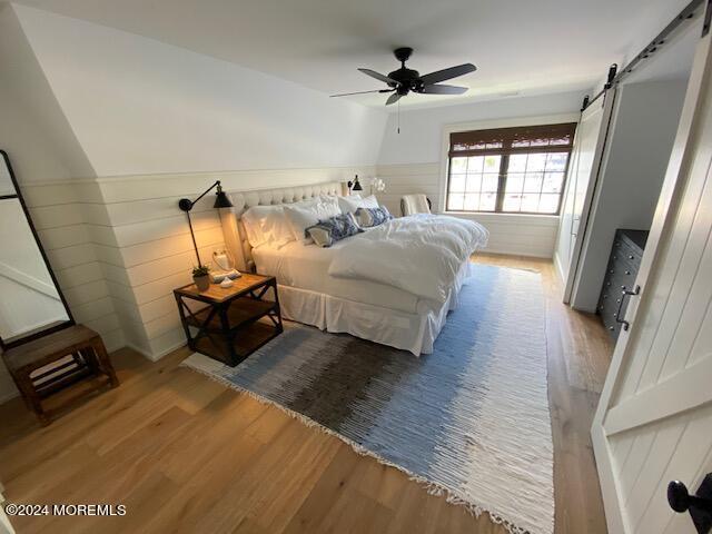 bedroom featuring a wainscoted wall, a barn door, and wood finished floors