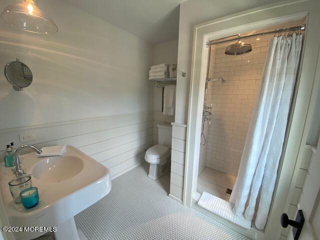 full bath with a sink, toilet, wainscoting, tile patterned floors, and a stall shower