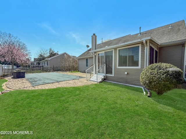 rear view of house featuring entry steps, a lawn, a chimney, fence, and a patio