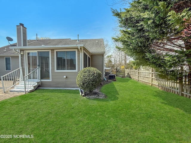 rear view of property with roof with shingles, a chimney, entry steps, a fenced backyard, and a lawn