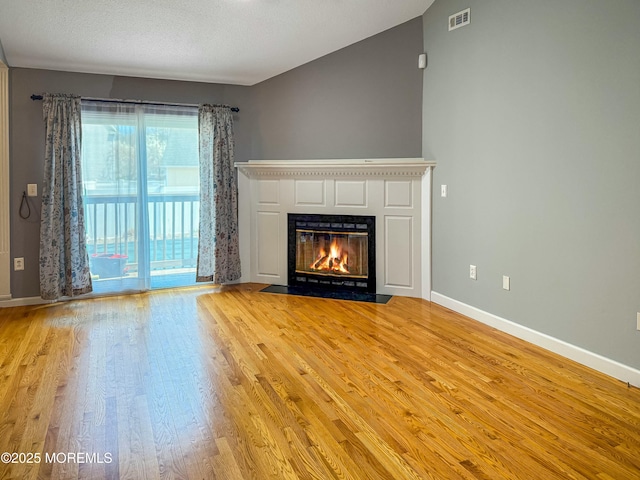 unfurnished living room with a fireplace with flush hearth, light wood finished floors, visible vents, and baseboards
