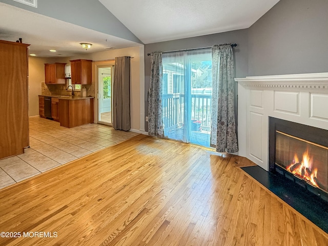 unfurnished living room with baseboards, a fireplace with flush hearth, visible vents, lofted ceiling, and light wood finished floors