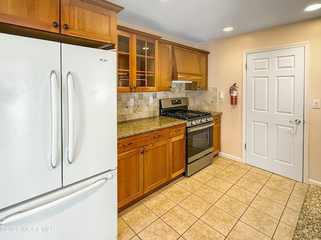 kitchen featuring brown cabinetry, stainless steel range with gas stovetop, freestanding refrigerator, and dark stone counters