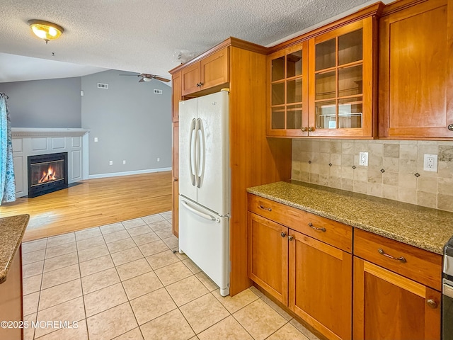kitchen featuring freestanding refrigerator, a ceiling fan, brown cabinets, backsplash, and light tile patterned flooring