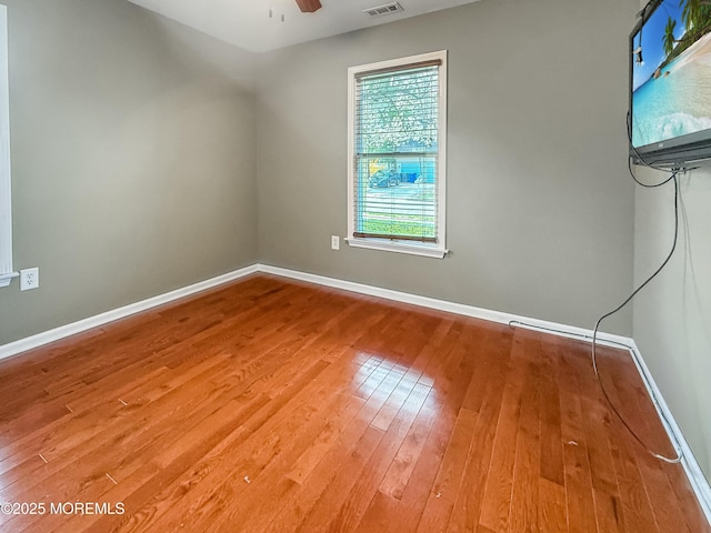 empty room with hardwood / wood-style floors, ceiling fan, baseboards, and visible vents
