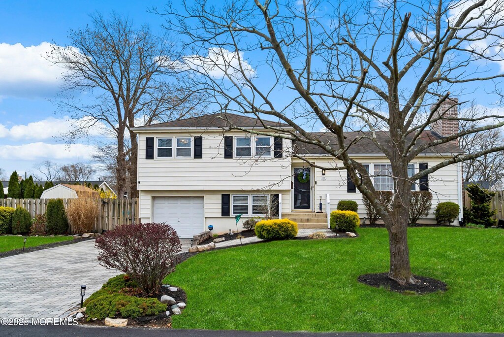 tri-level home featuring a chimney, driveway, a front yard, a garage, and fence