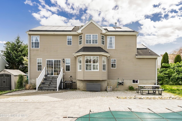 rear view of house featuring a covered pool, a patio area, an outdoor structure, a storage shed, and roof mounted solar panels