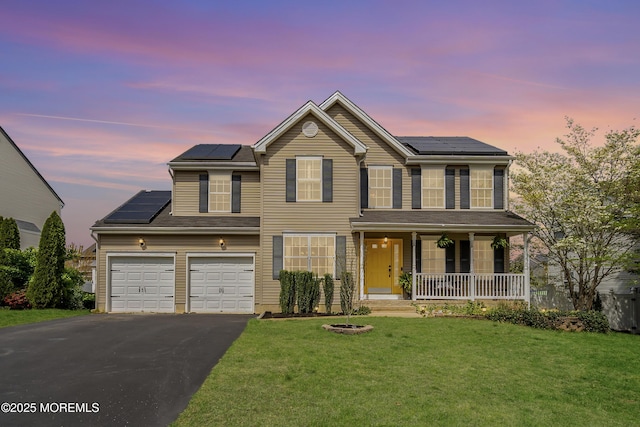 traditional-style home with a porch, a lawn, roof mounted solar panels, and aphalt driveway
