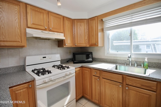 kitchen with white gas range oven, black microwave, under cabinet range hood, a sink, and backsplash