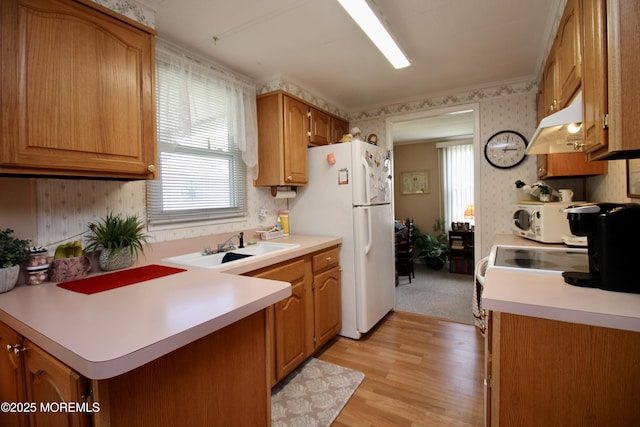 kitchen featuring white appliances, under cabinet range hood, light countertops, a sink, and wallpapered walls