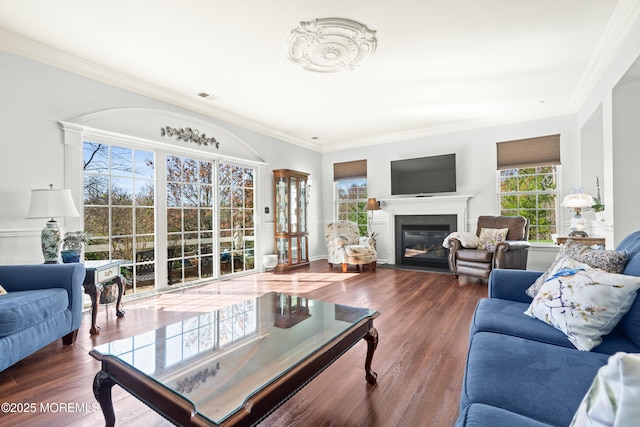 living room featuring a glass covered fireplace, visible vents, ornamental molding, and wood finished floors