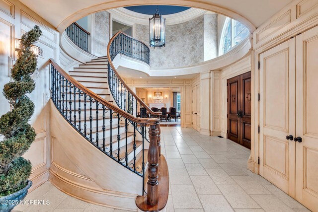 entryway featuring a high ceiling, an inviting chandelier, a decorative wall, ornamental molding, and stairs