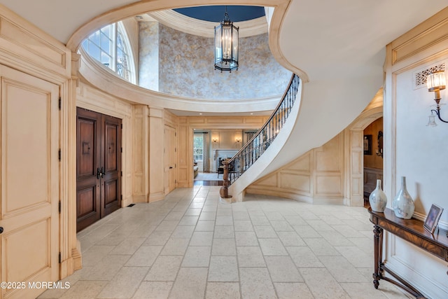 foyer featuring an inviting chandelier, ornamental molding, stairway, a high ceiling, and a decorative wall