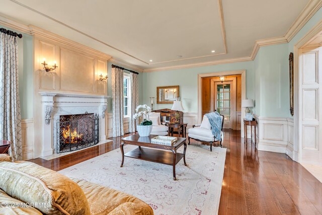 living area with a high end fireplace, ornamental molding, a decorative wall, and wood finished floors