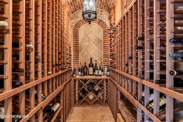 wine room featuring brick ceiling, a notable chandelier, vaulted ceiling, and stone tile floors