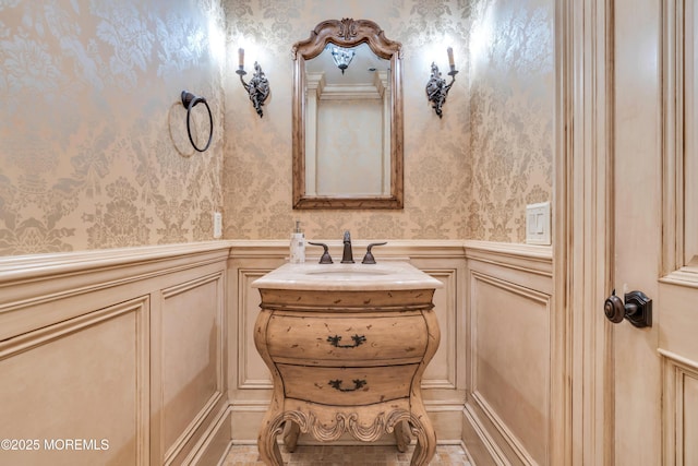 bathroom with wallpapered walls, vanity, wainscoting, and a decorative wall