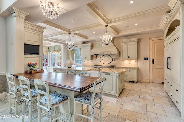 kitchen with custom range hood, a center island with sink, an inviting chandelier, and cream cabinetry