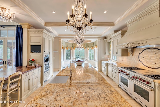 kitchen with a chandelier, a tray ceiling, range with two ovens, and cream cabinets