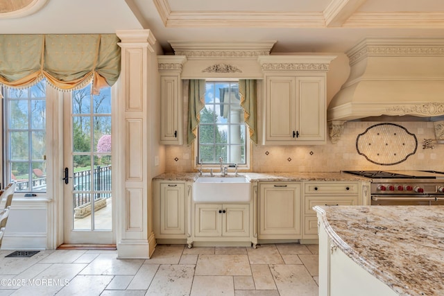 kitchen with custom exhaust hood, tasteful backsplash, a sink, and cream cabinetry