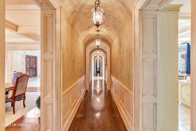 hall with a notable chandelier, dark wood-style flooring, vaulted ceiling, a decorative wall, and arched walkways