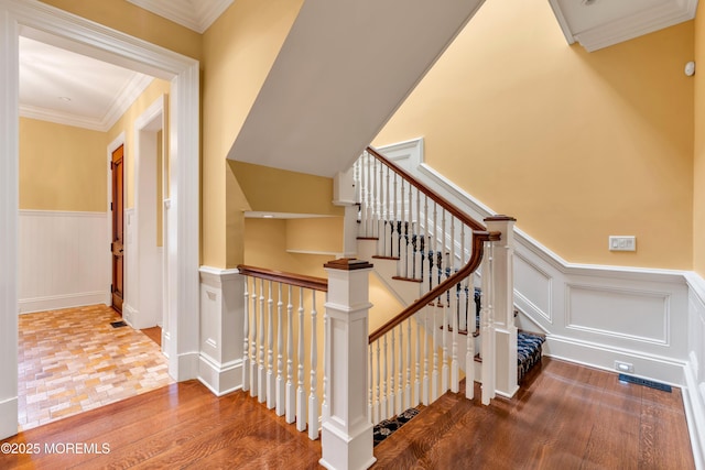 stairway featuring ornamental molding, wainscoting, and wood finished floors