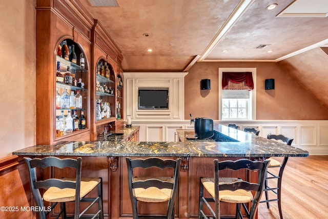 bar with a decorative wall, wet bar, ornamental molding, wainscoting, and light wood finished floors