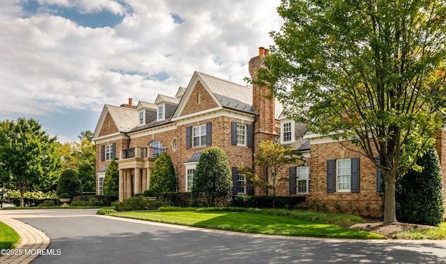 colonial inspired home with a chimney, a front yard, and brick siding