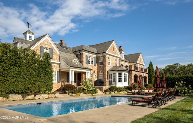 rear view of house with a patio area, an outdoor pool, brick siding, and a chimney