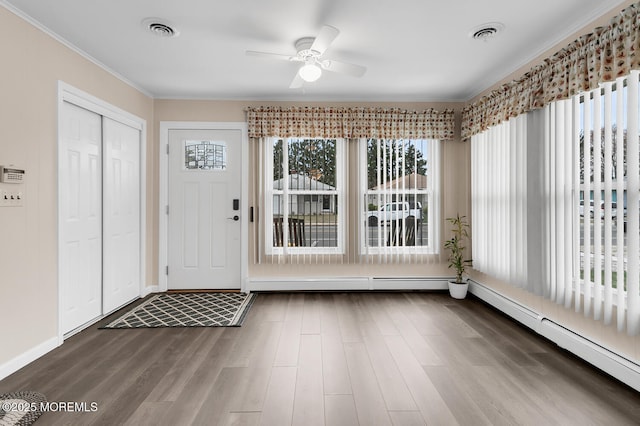 foyer entrance with a baseboard heating unit, a ceiling fan, crown molding, visible vents, and wood finished floors