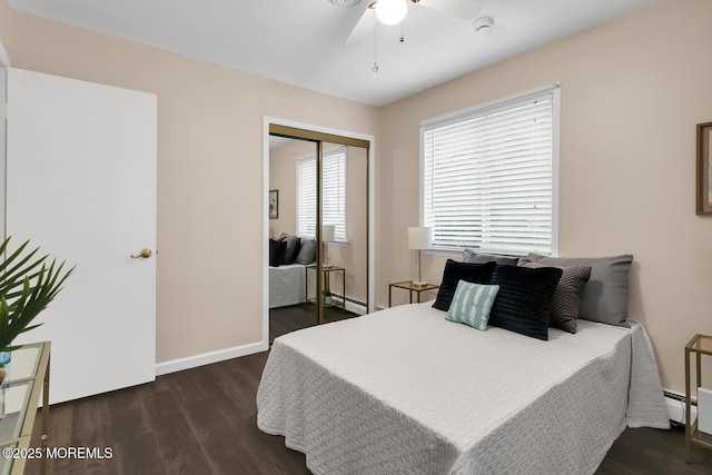 bedroom featuring a baseboard heating unit, a closet, baseboards, a ceiling fan, and wood finished floors