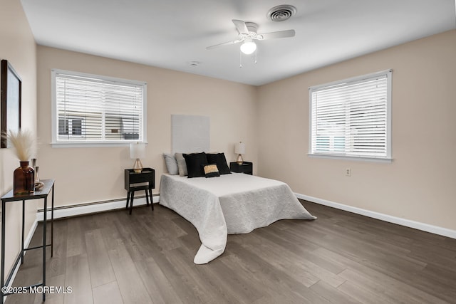 bedroom with visible vents, multiple windows, a baseboard heating unit, and dark wood finished floors