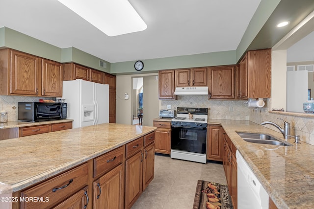 kitchen featuring white appliances, under cabinet range hood, a sink, light stone countertops, and decorative backsplash