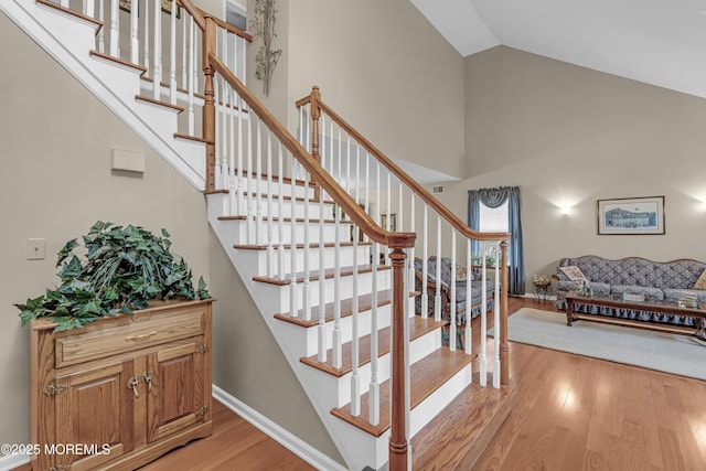 stairs featuring wood finished floors, high vaulted ceiling, and baseboards
