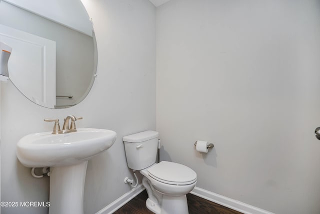 half bathroom with baseboards, toilet, and wood finished floors